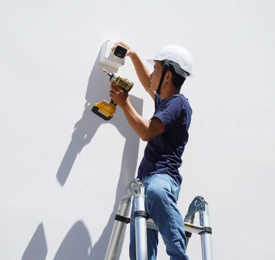 Technician on ladder performing CCTV maintenance on outdoor camera