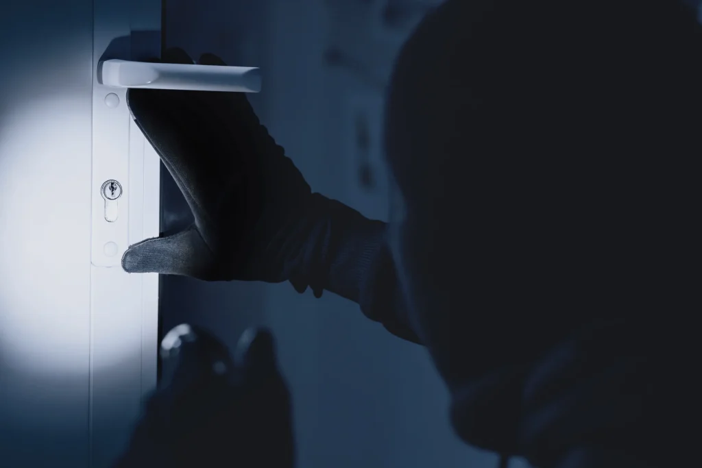 A masked figure attempting to unlock a white door, demonstrating the importance of home security systems.